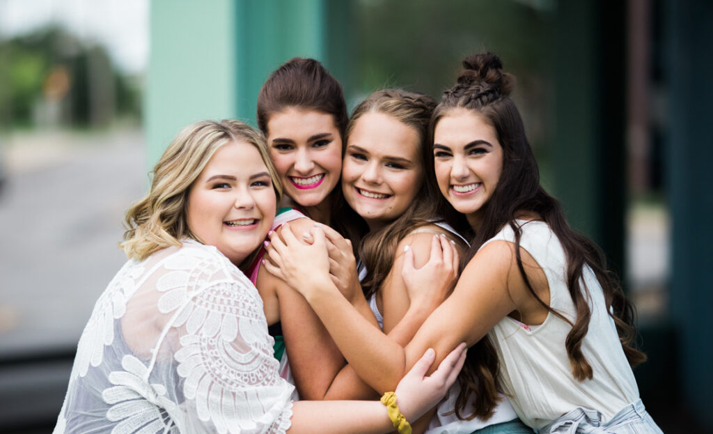 a group of high school girls embrace during a photoshoot in downtown fort wayne