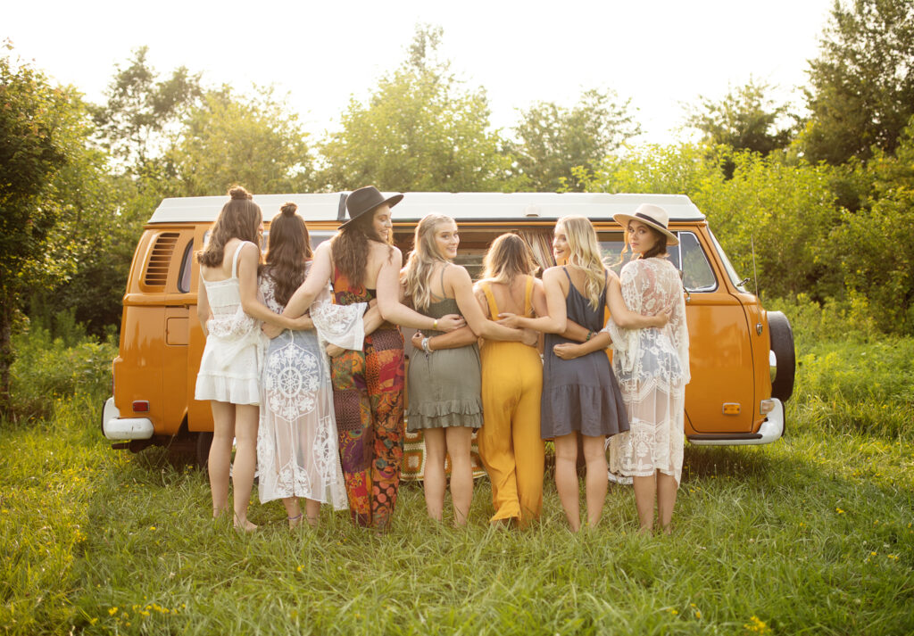 a group of girls look over their shoulders at the camera during a retro styled photoshoot with a vintage volkswagon bus in a field in fort wayne