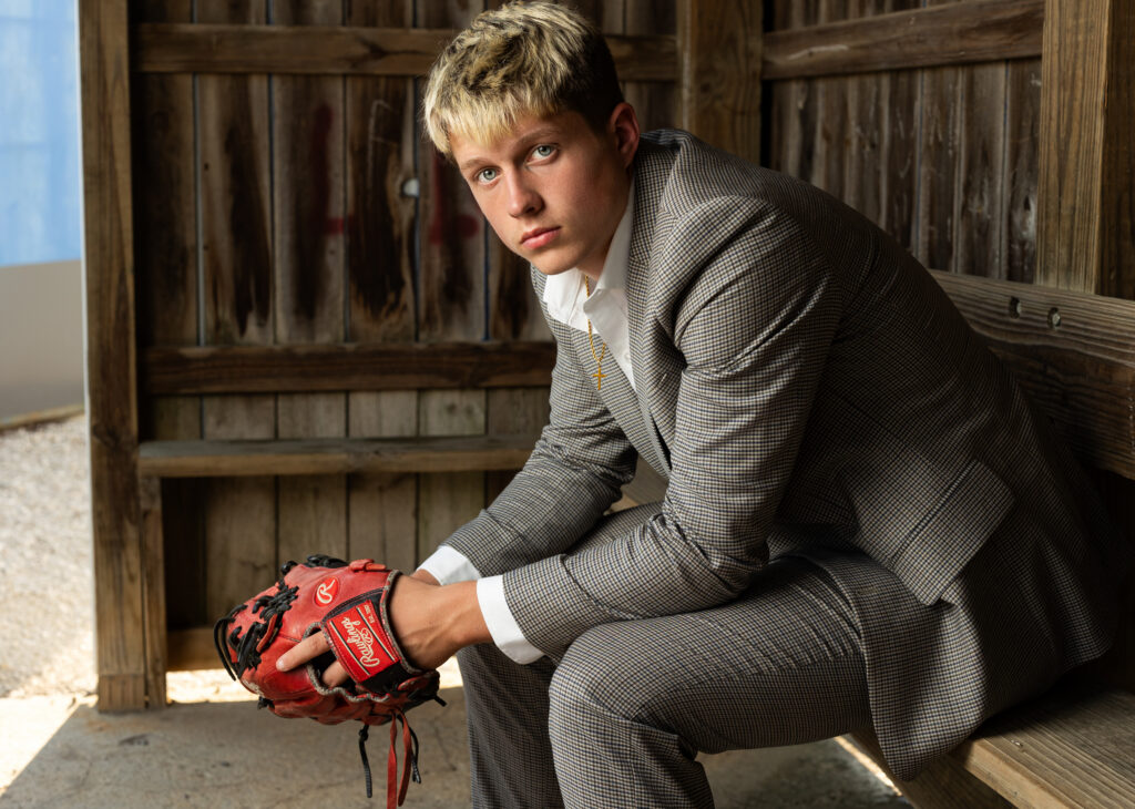 Senior wearing a suit in the baseball dugout, adding a stylish twist to traditional sports photography.